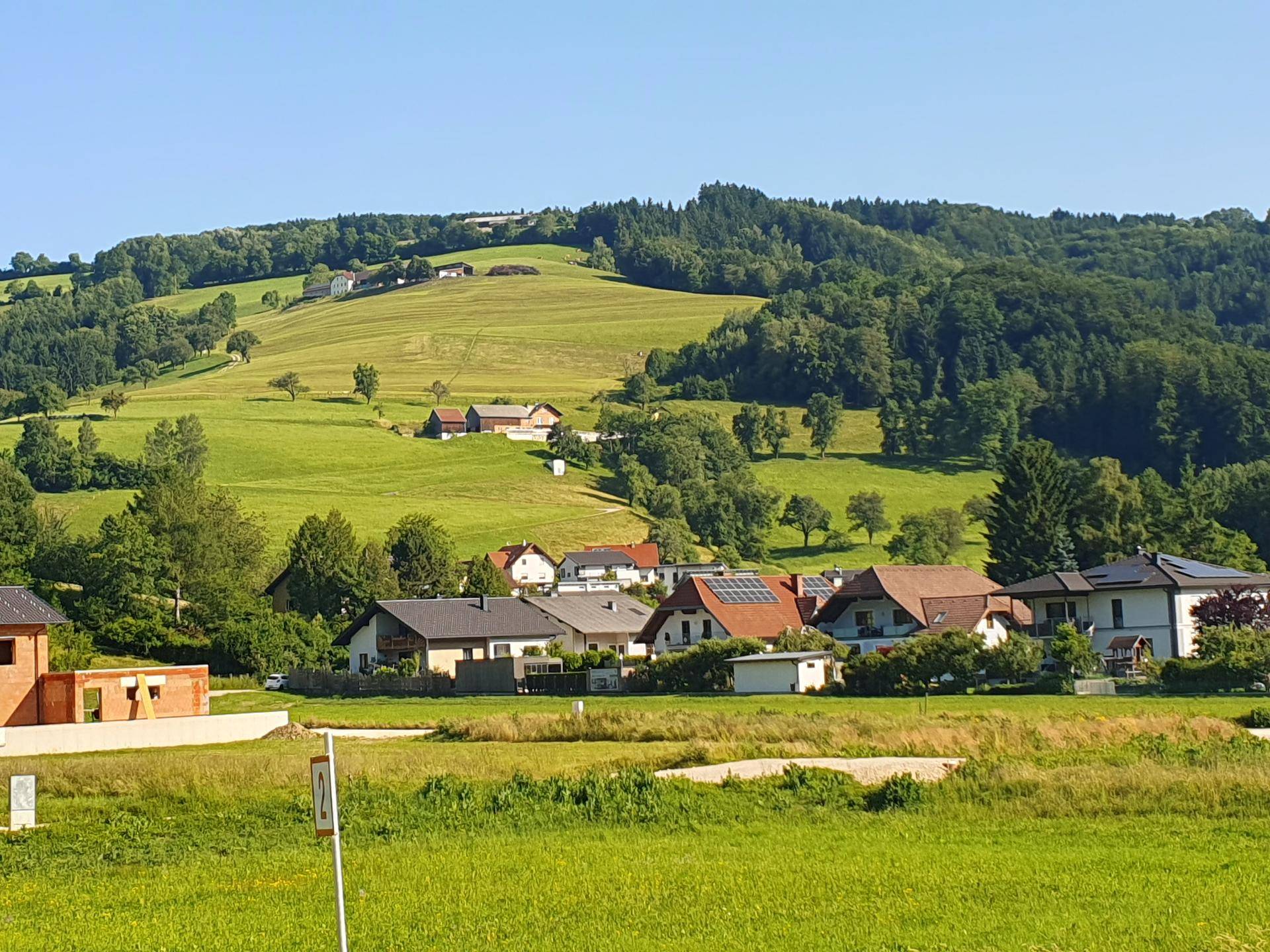 Weitläufiger Blick über sanfte grüne Hügel, Felder und eine ländliche Siedlung.