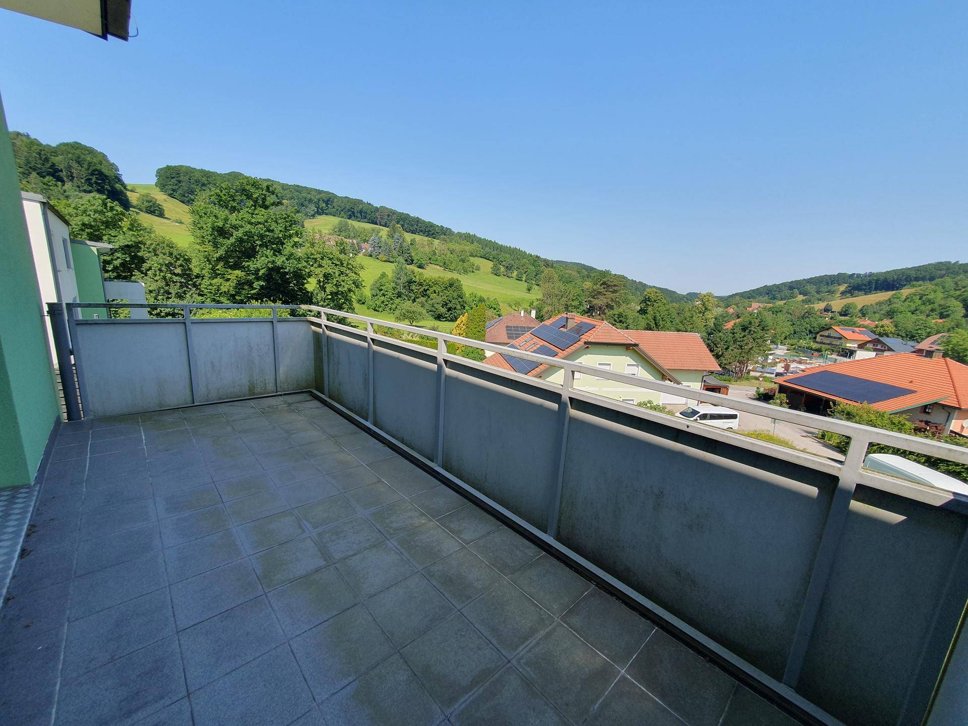 Geräumiger Balkon mit Fliesenboden und weitem Blick über grüne Hügel und Dächer.