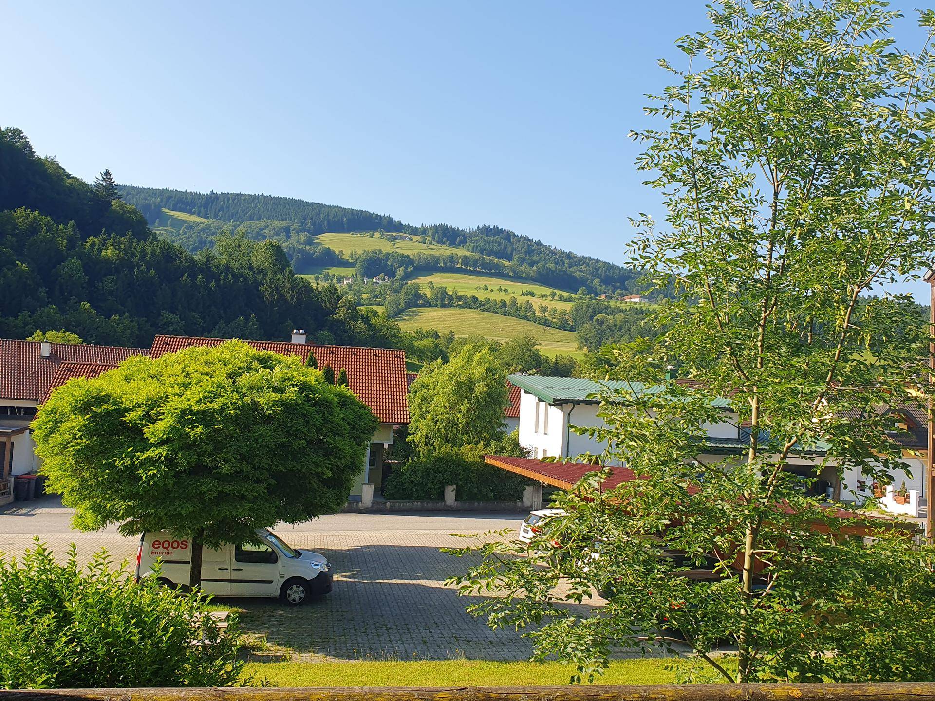 Blick auf grüne Hügel und bewaldete Landschaft mit einigen Häusern im Vordergrund.