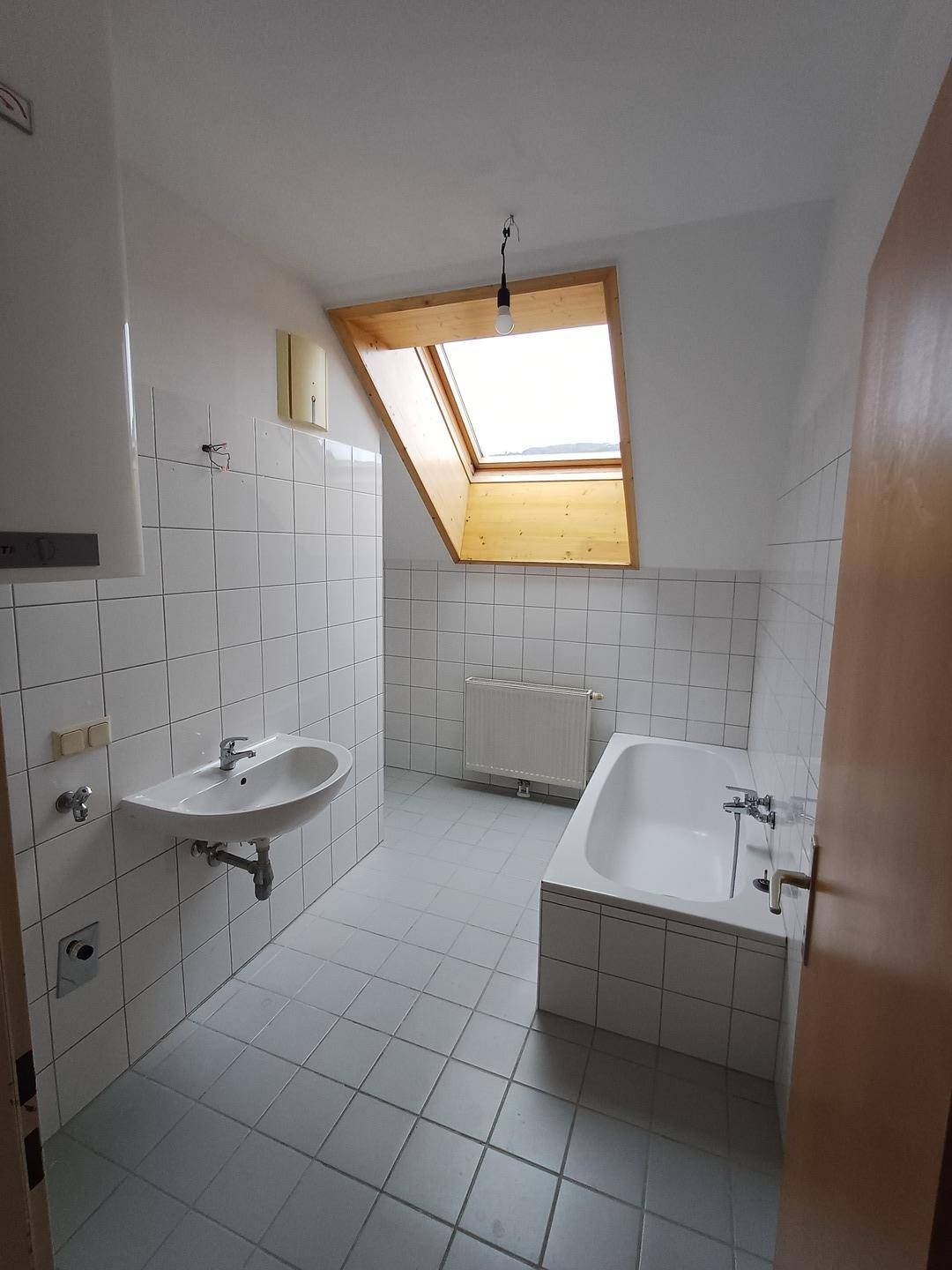 Gefliestes Badezimmer im Dachgeschoss mit Badewanne, Waschbecken und Dachfenster.