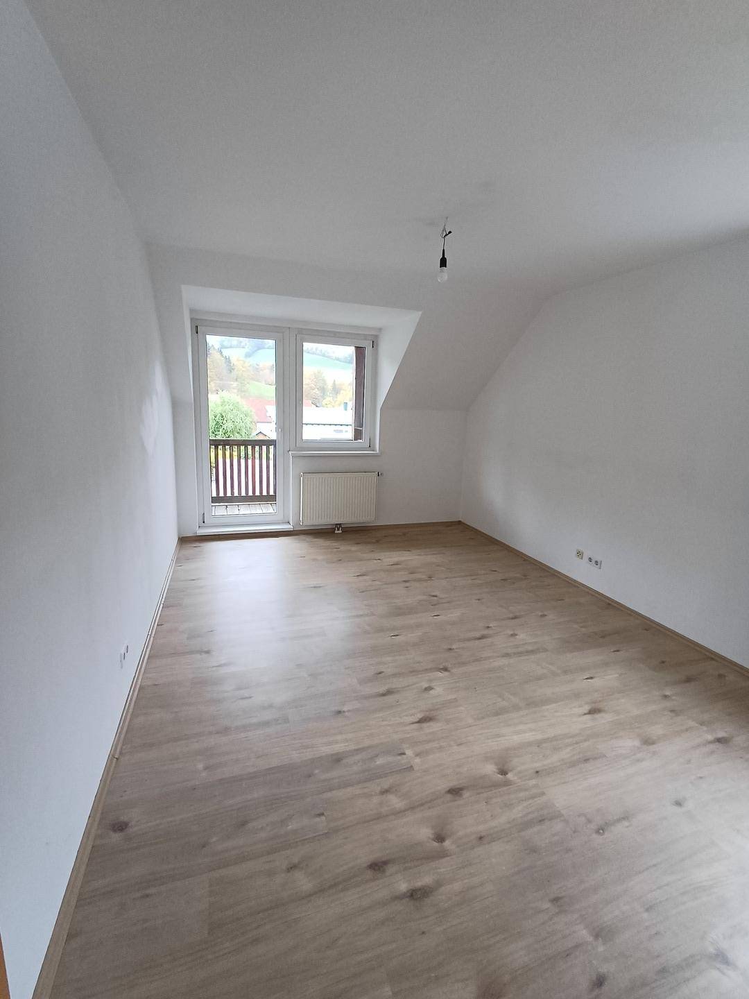 Heller, leerer Raum mit Laminatboden, weißen Wänden und Zugang zu einem kleinen Balkon.