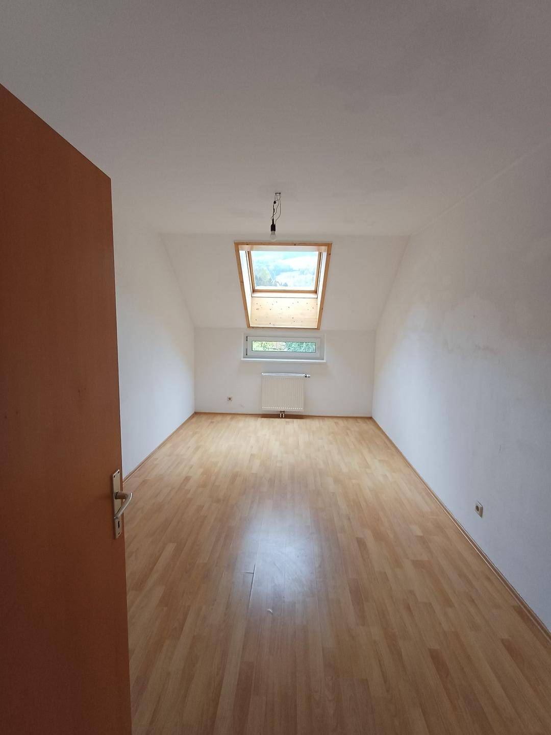 Helles Zimmer im Dachgeschoss mit Laminatboden und Dachfenster für viel Tageslicht.