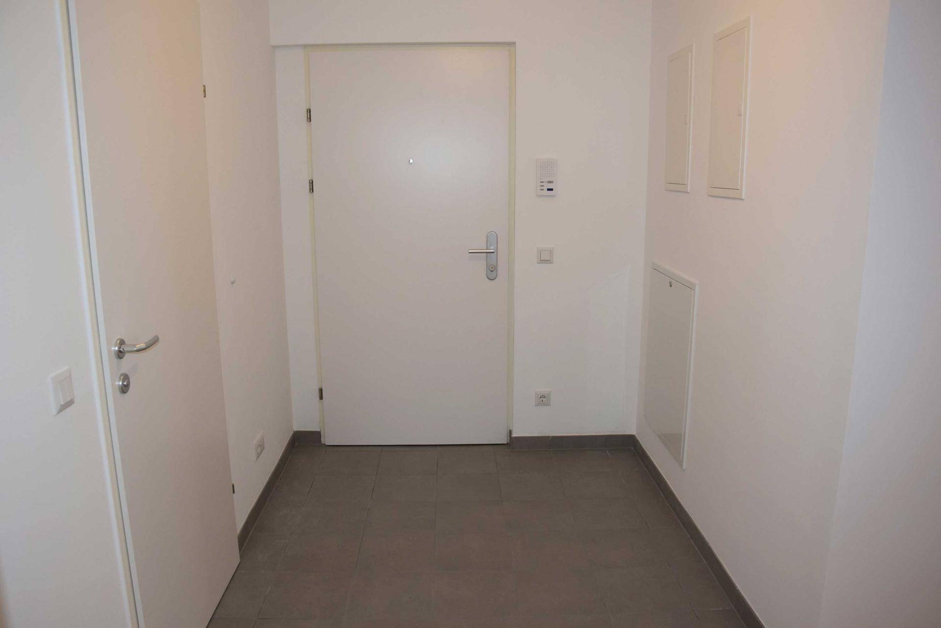 Heller Eingangsbereich mit weiß gestrichenen Wänden und modernen grauen Fliesenboden.