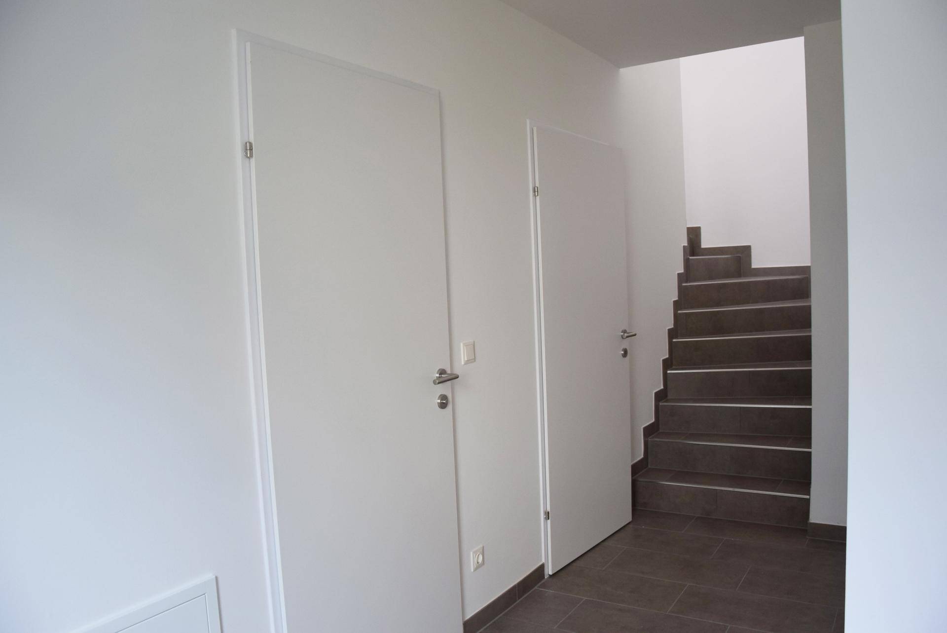 Heller Flur mit dunklen Fliesen und Treppenaufgang in die obere Etage.