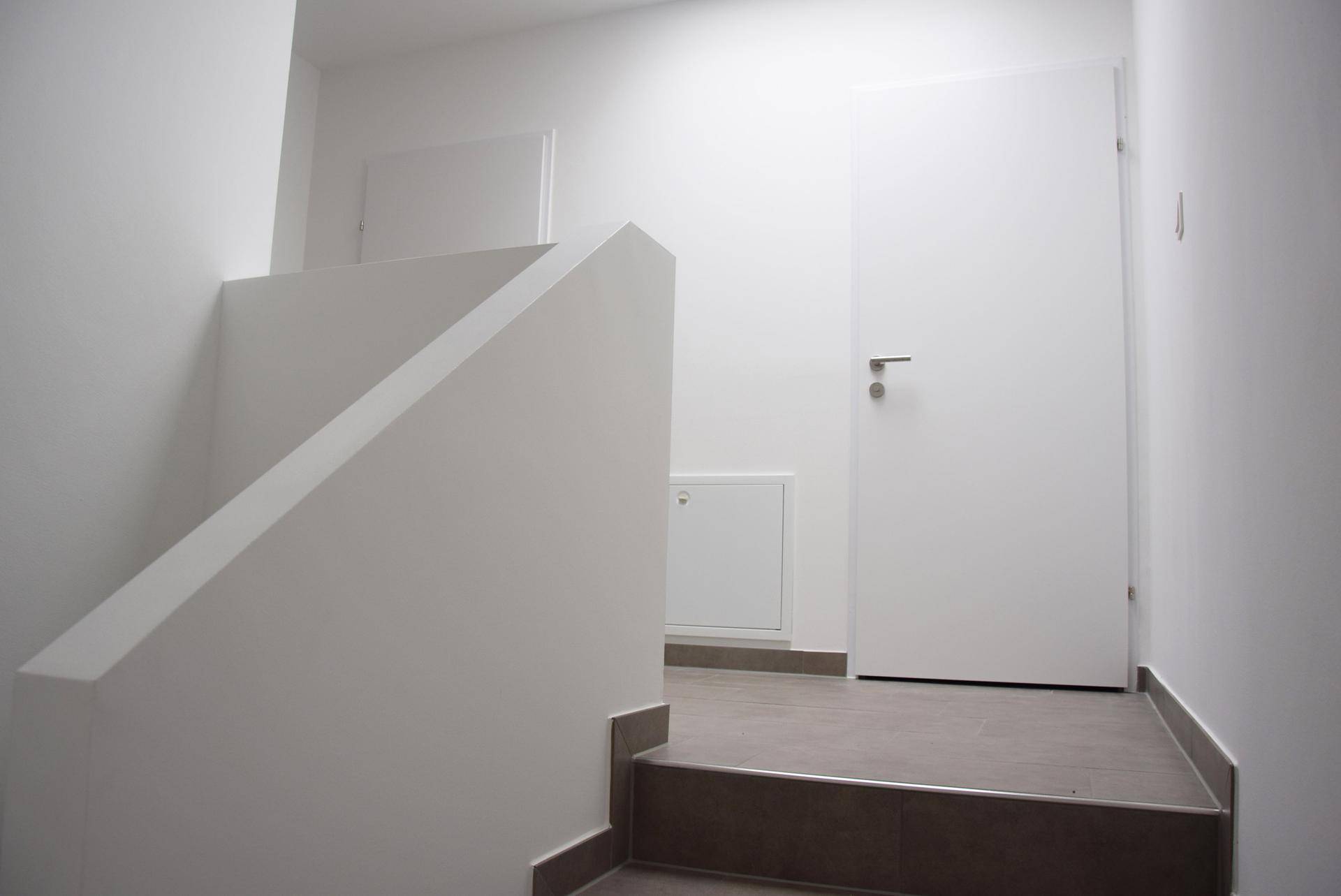 Moderner Treppenaufgang in einem hellen Flur mit schlichten weißen Wänden.