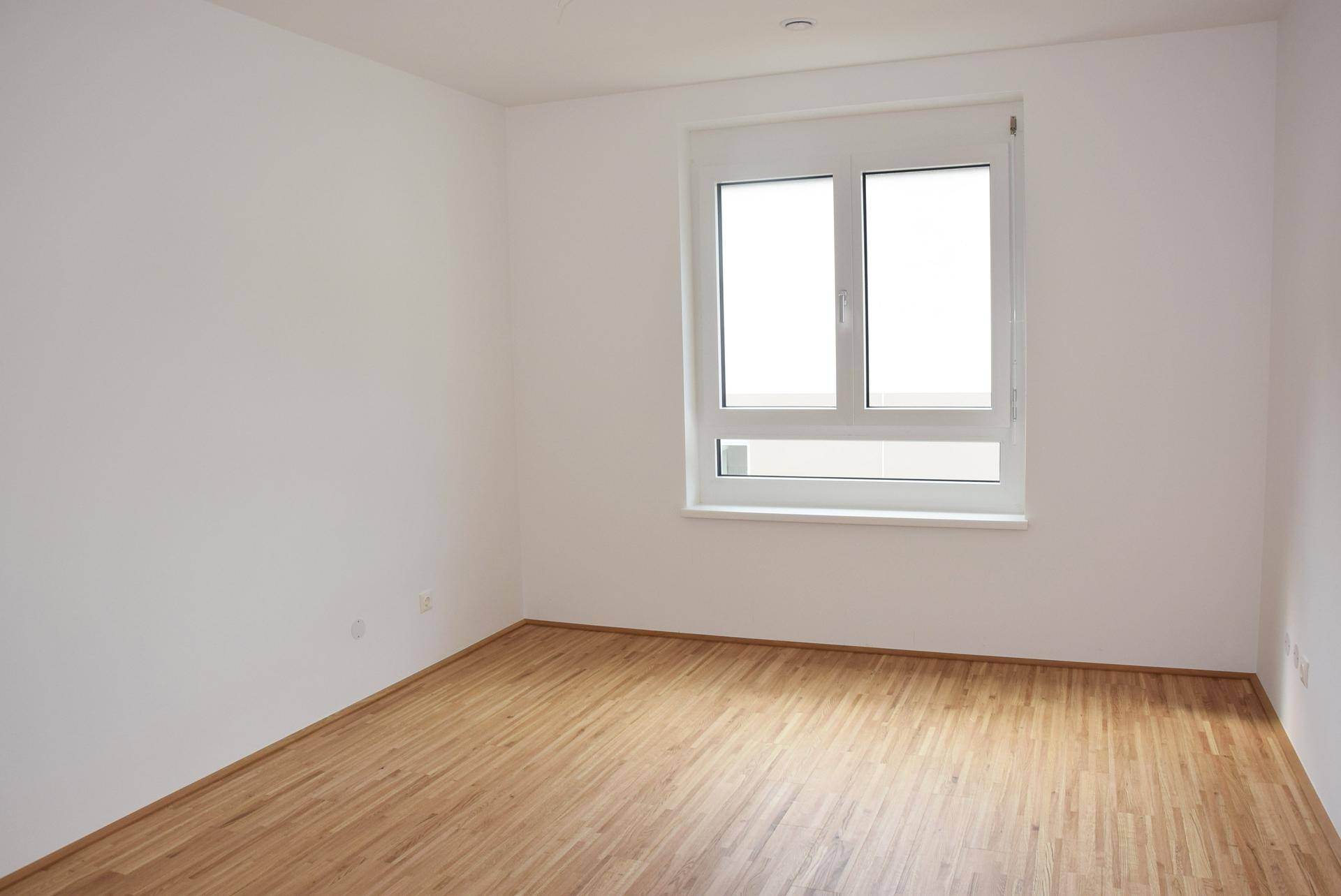 Helles Zimmer mit Parkettboden und großem Fenster, ideal als Schlafzimmer.