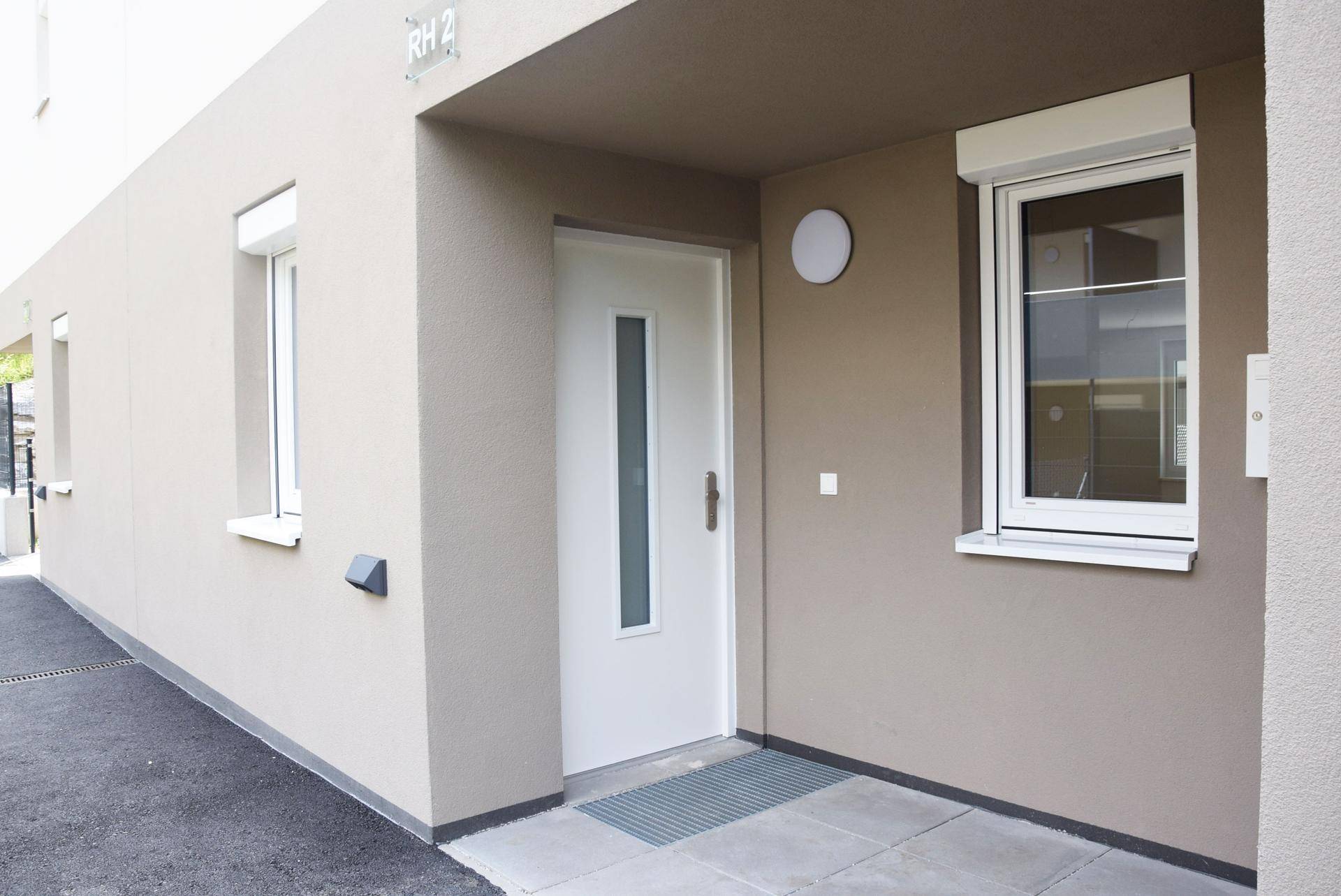 Eingangsbereich eines modernen Reihenhauses mit beiger Fassade und Rollläden.