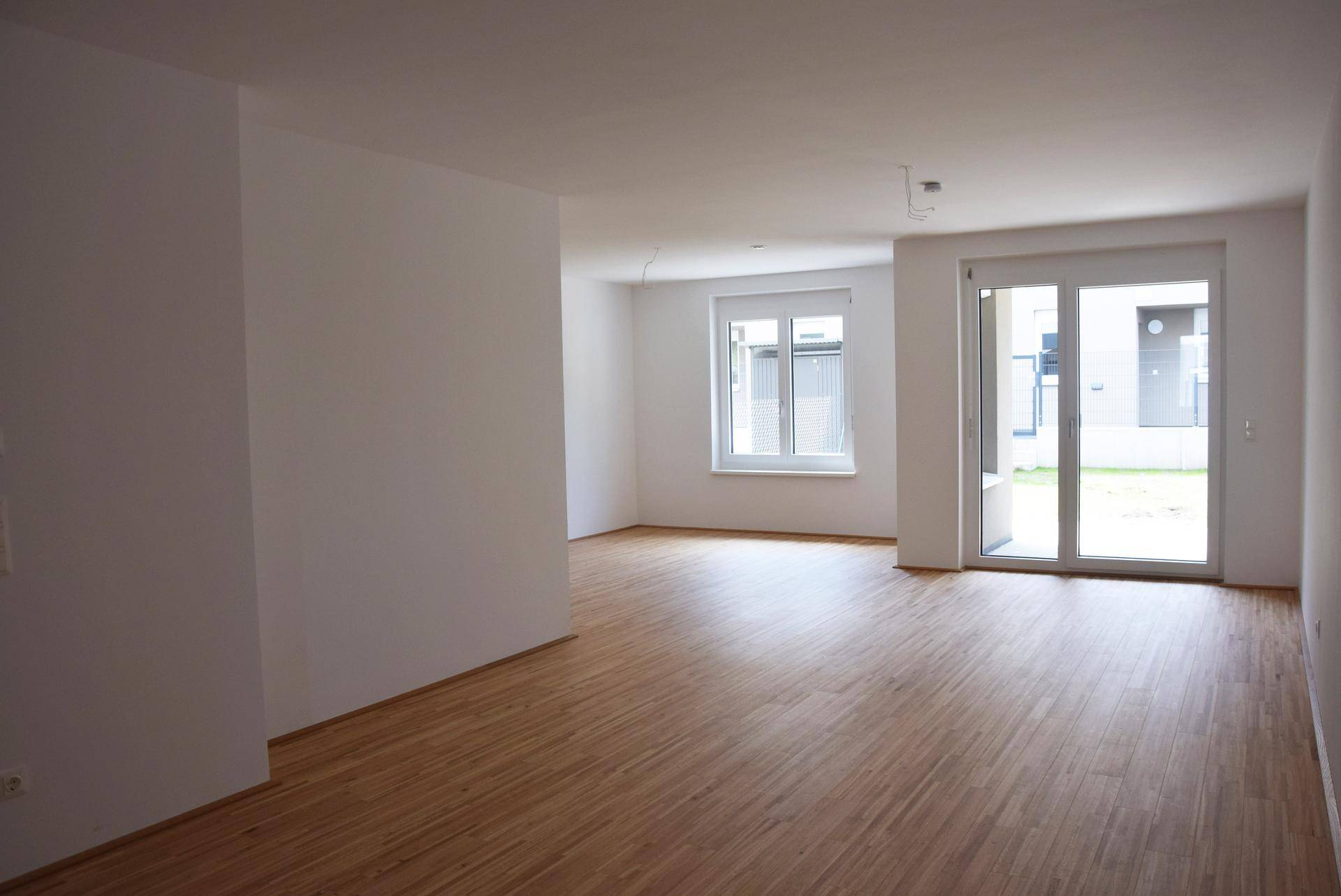 Geräumiger, heller Wohnbereich mit Parkettboden und Zugang zur Terrasse.