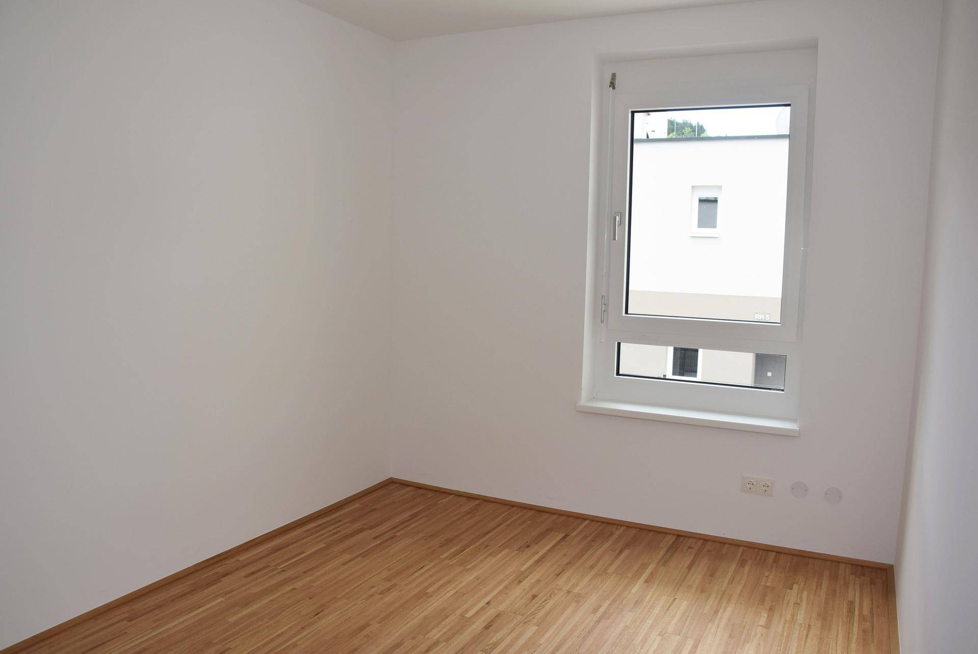 Freundliches Zimmer mit Parkettboden und Fenster, das viel Tageslicht hereinlässt.