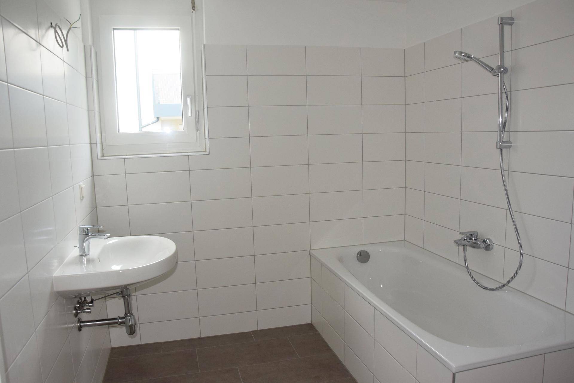 Modernes Badezimmer mit weißen Fliesen, Badewanne und Fenster für Tageslicht.