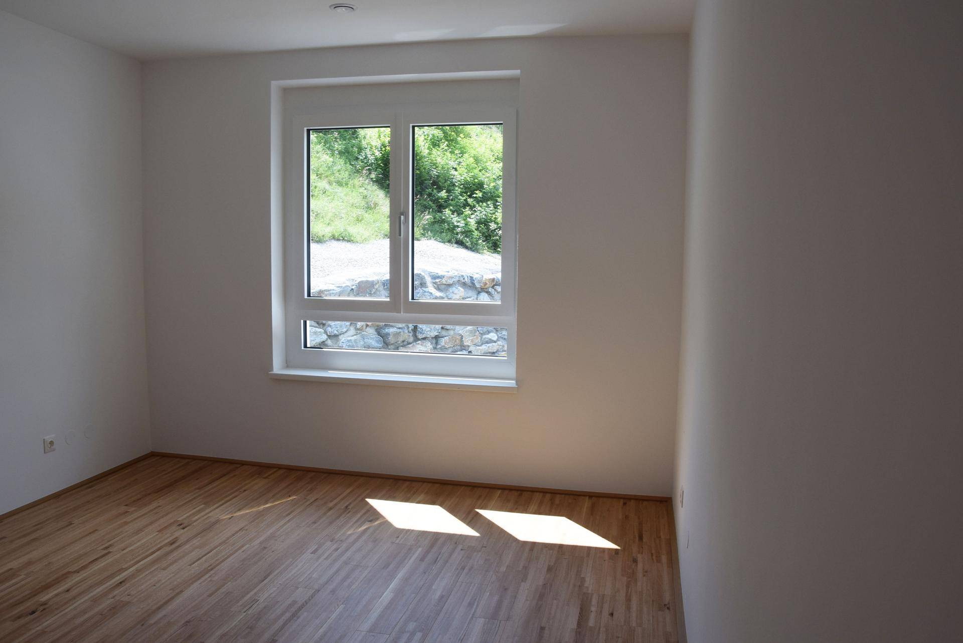 Helles Schlafzimmer mit Holzboden und Fenster, das einen Blick ins Grüne bietet.