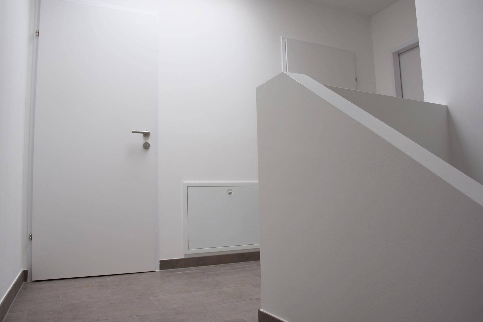 Moderner Treppenaufgang in einem hellen Flur mit weißen Wänden und Fliesenboden.