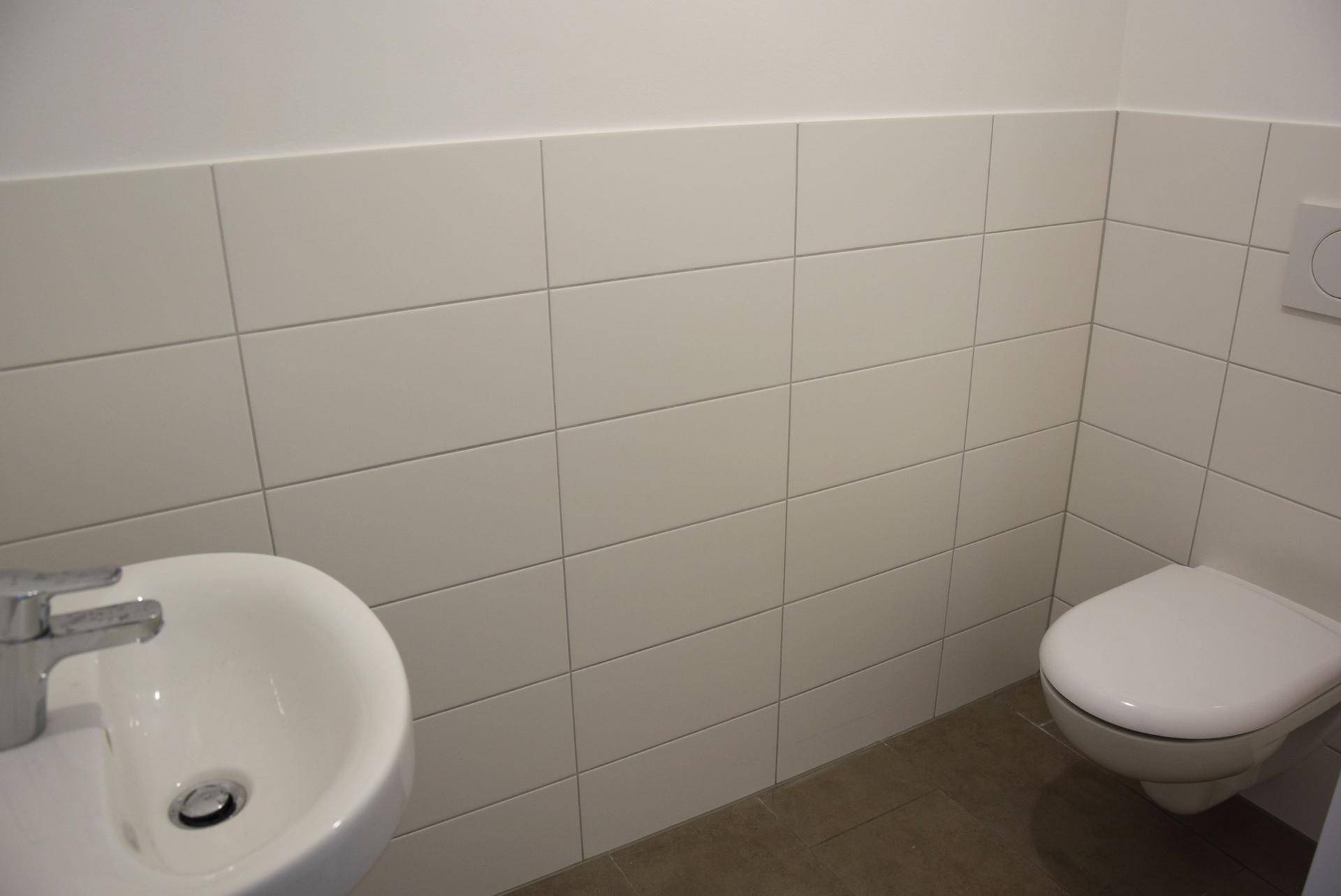 Separates Gäste-WC mit wandhängender Toilette, kleinem Waschbecken und Fliesen.