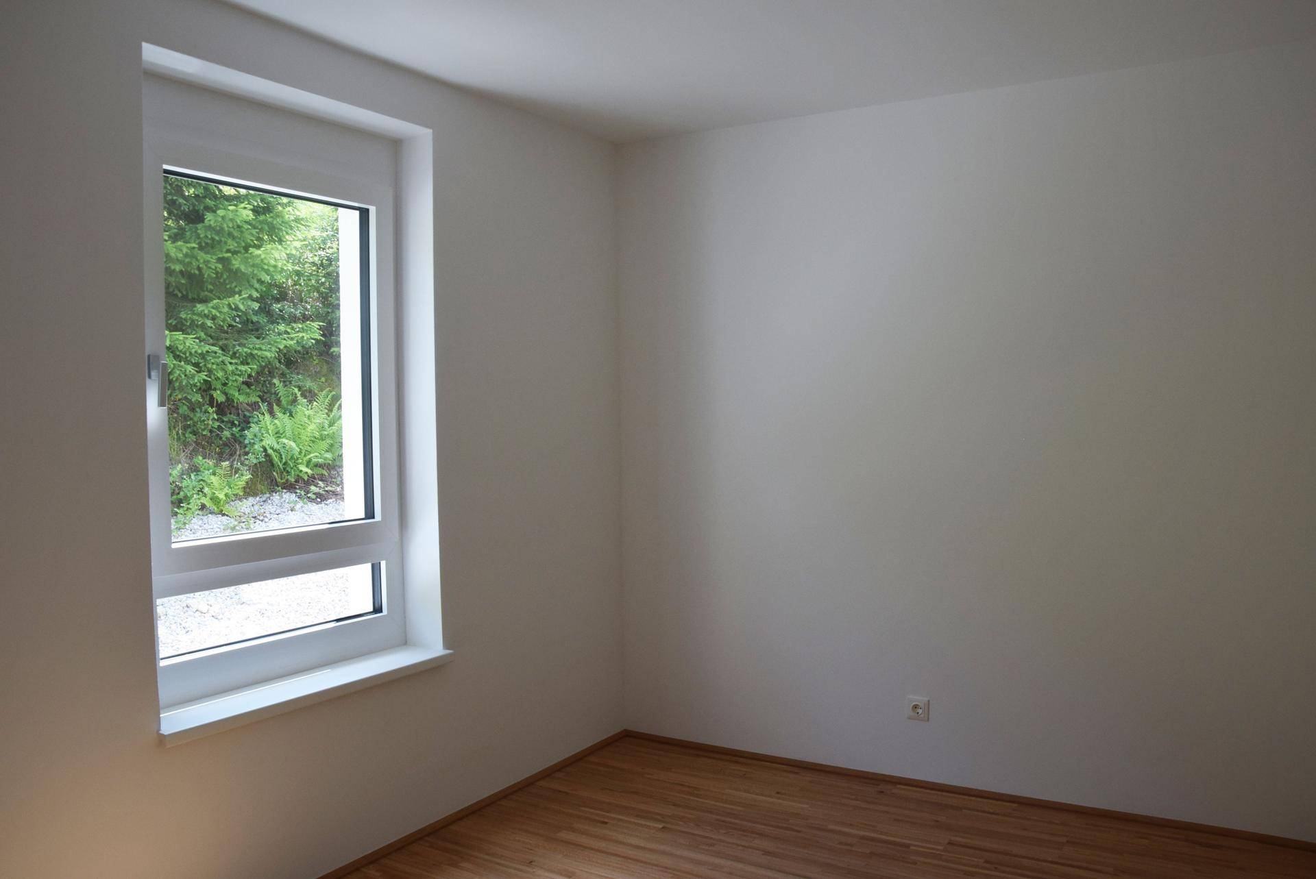 Schlichtes Zimmer mit Holzboden und Fenster mit Blick auf die umliegende Natur.