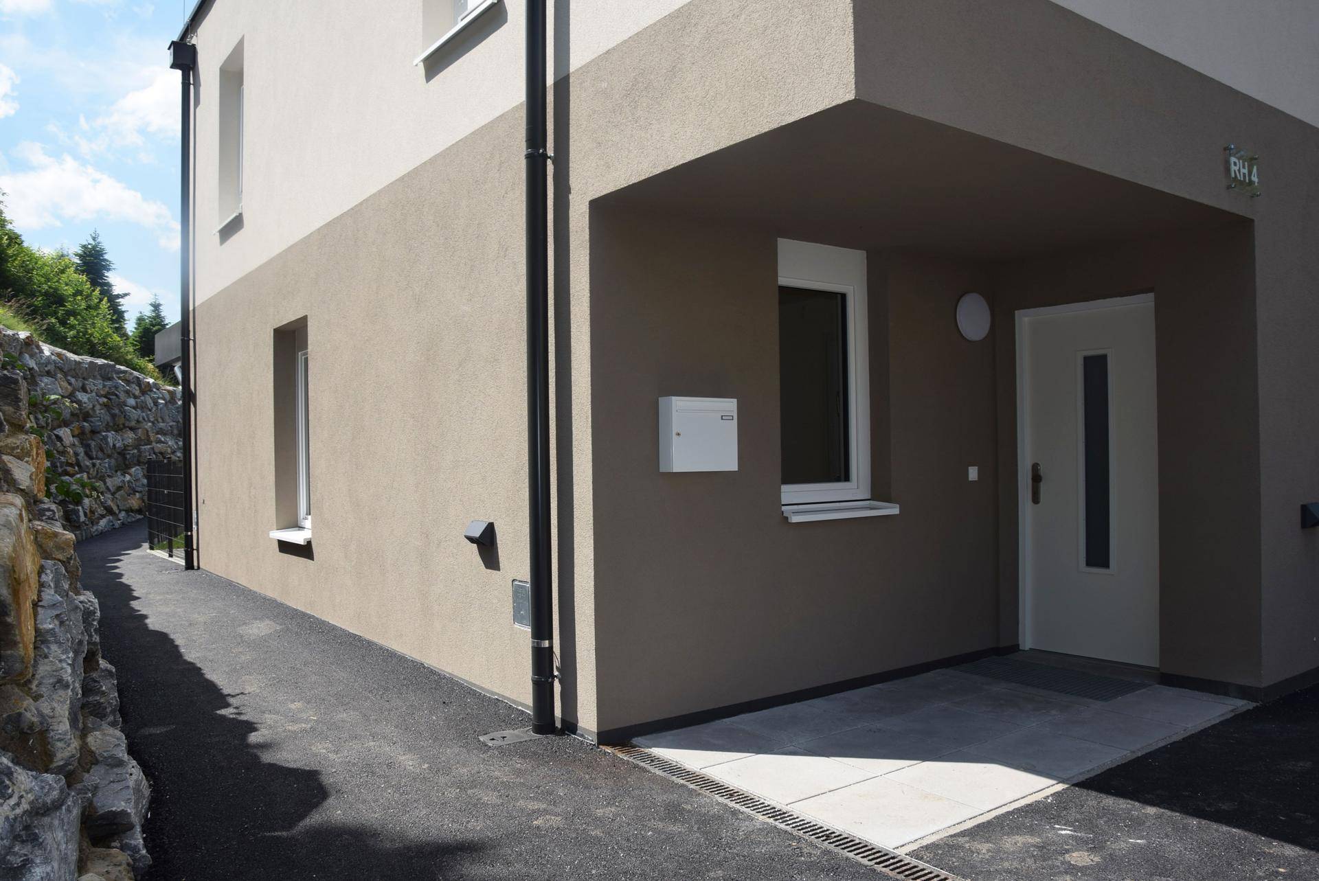 Eingangsbereich eines modernen Neubaus mit zweifarbiger Fassade und überdachtem Zugang.