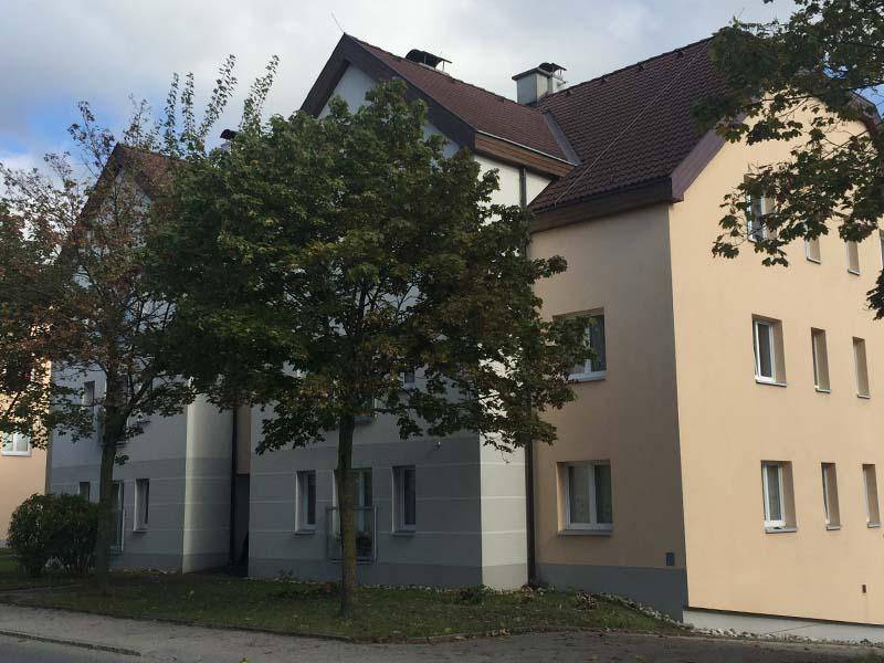 Seitenansicht des Wohngebäudes mit gepflegter Fassade, Fenstern und grünen Bäumen im Vordergrund.