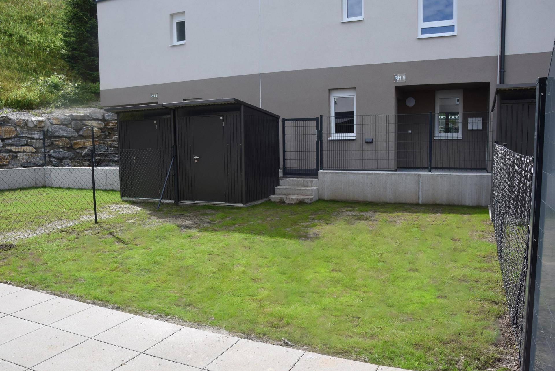 Kleiner Gartenbereich mit Rasenfläche und zwei praktischen Abstellschuppen.
