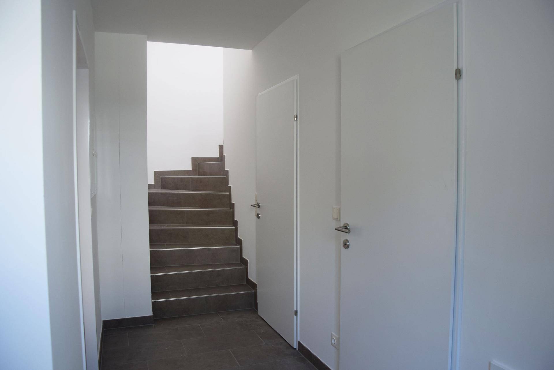 Heller Flur mit Treppenaufgang und schlichten weißen Türen in einem modernen Neubau.