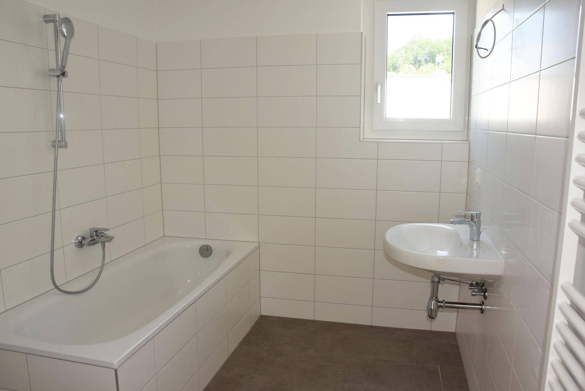 Modernes Badezimmer mit Badewanne, Waschbecken, weißen Fliesen und Fenster.