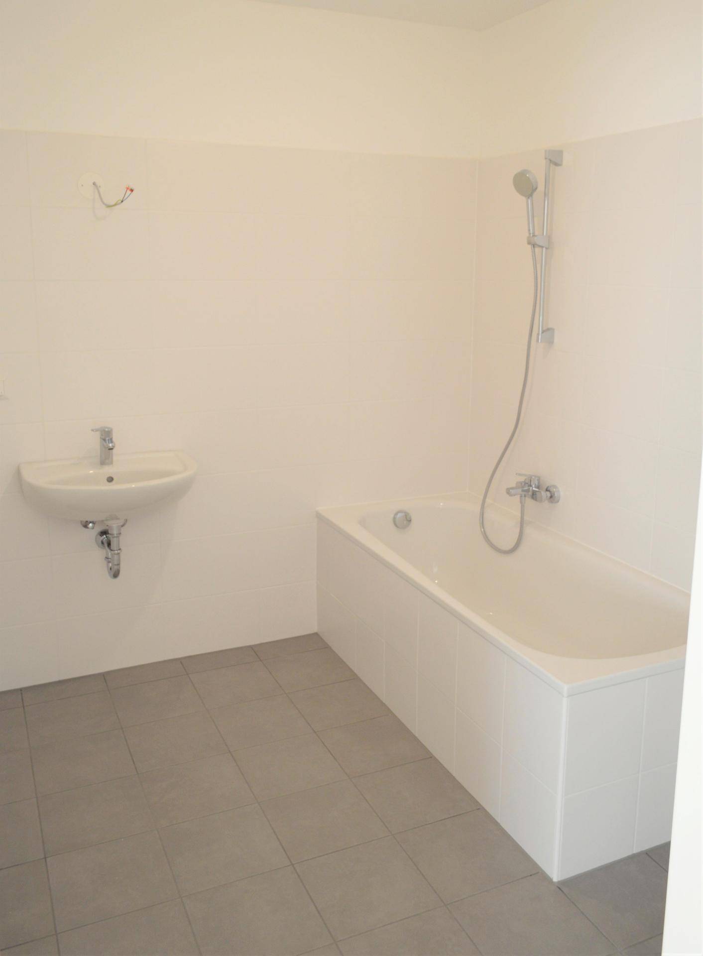 Modernes Badezimmer mit Badewanne, Waschbecken und grauen Fliesen, bereit zur Fertigstellung.