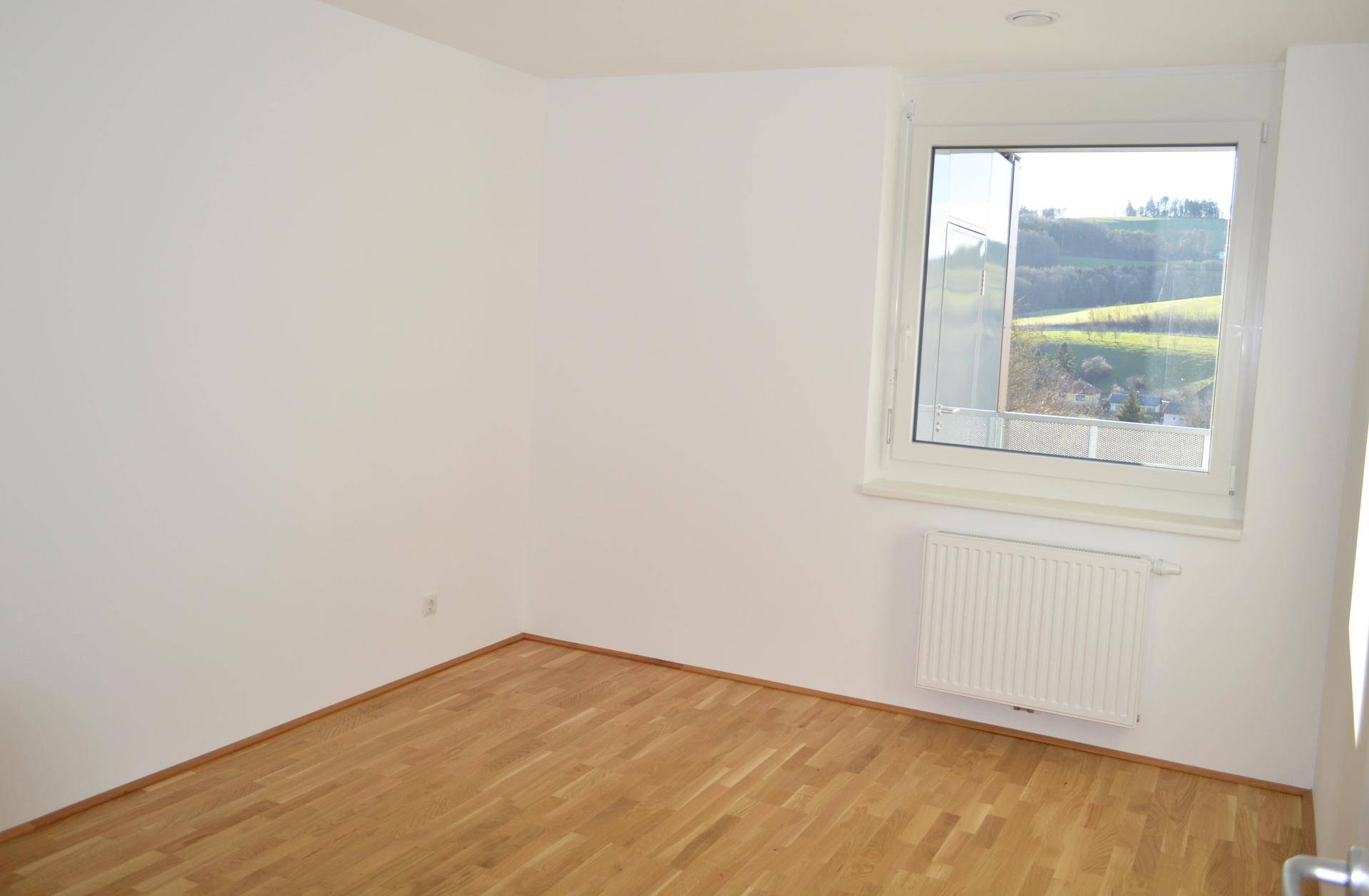 Schlafzimmer mit Holzboden und Fenster, das einen weiten Blick auf die grüne Landschaft bietet.