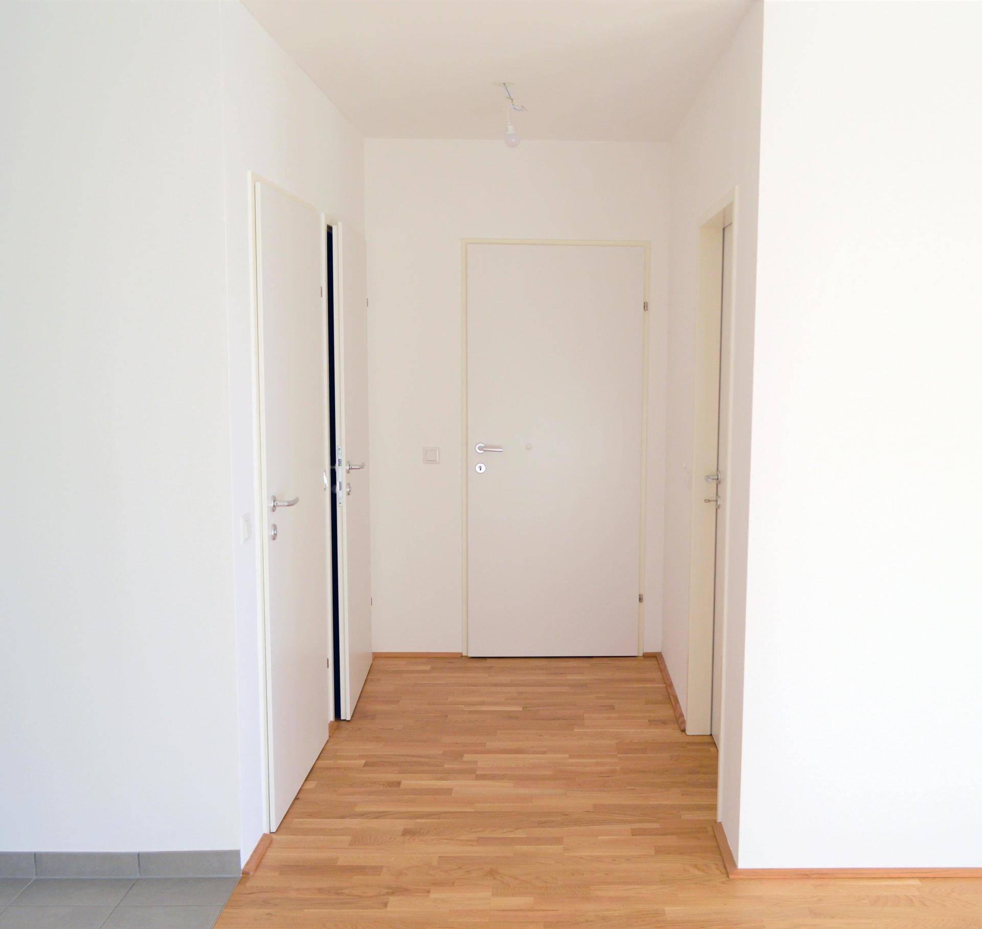 Heller Flur mit Holzboden und mehreren Türen, der verschiedene Räume verbindet.
