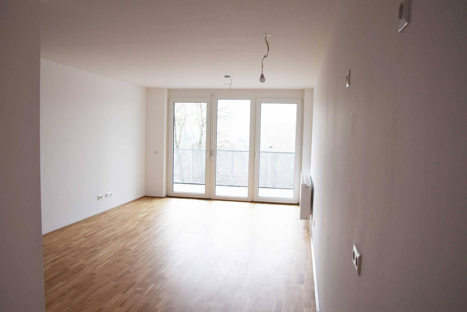 Lichtdurchfluteter Wohnraum mit Holzboden und großen Fenstern zum Balkon oder zur Terrasse.