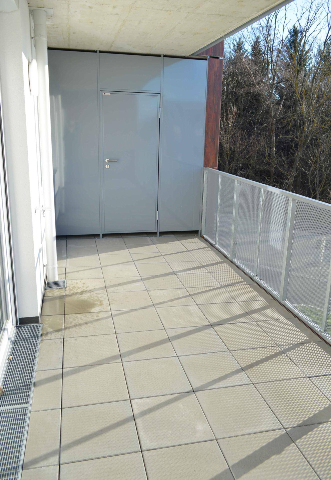 Geräumiger Balkon mit Fliesenboden und Metallgeländer, umgeben von Bäumen und Natur.