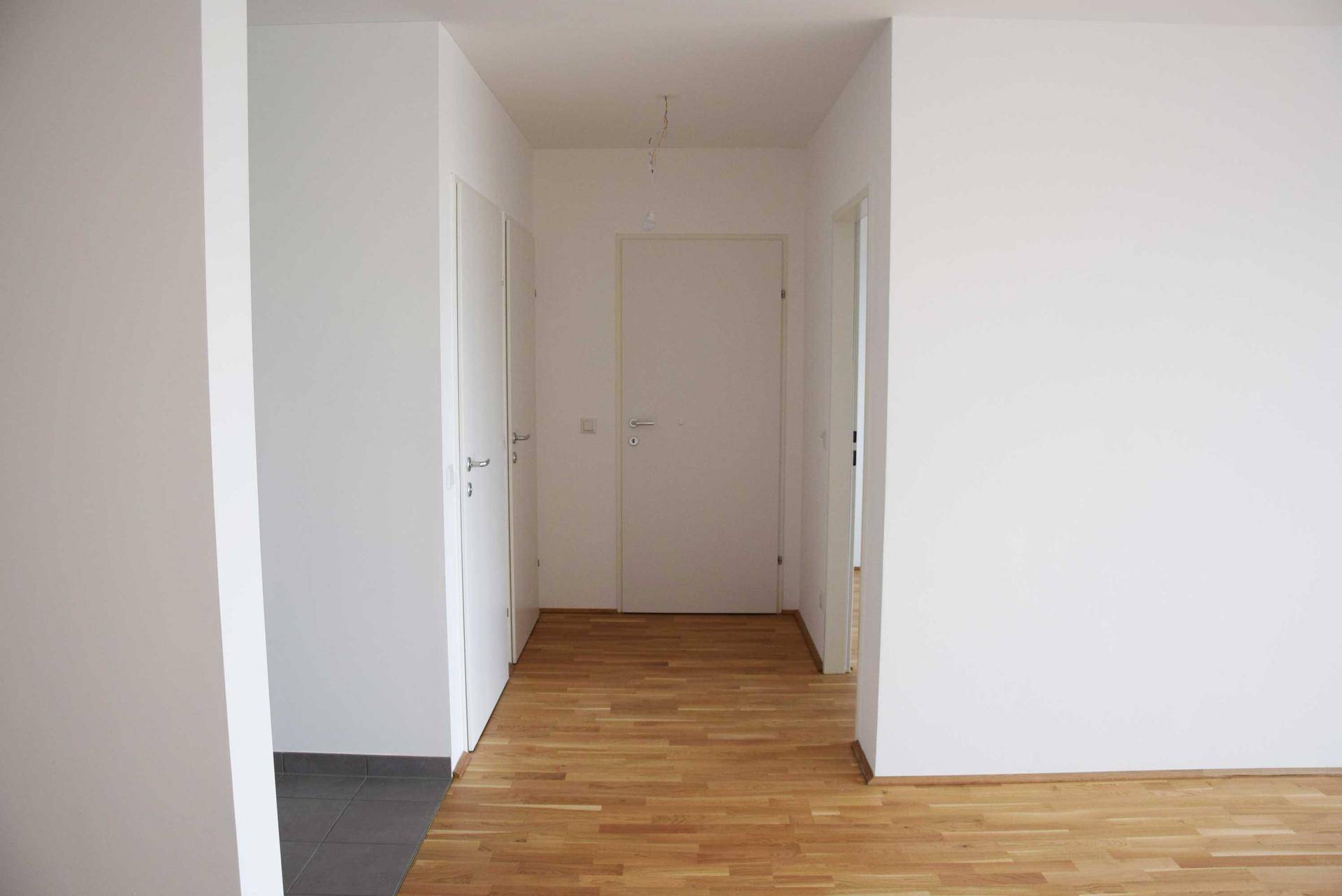 Heller Flur mit Holzboden und mehreren weißen Türen, der verschiedene Räume verbindet.