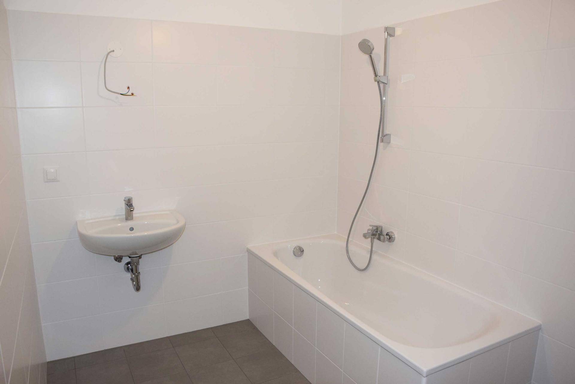 Modernes Badezimmer mit weißen Fliesen, Badewanne mit Duschfunktion und einem Waschbecken.