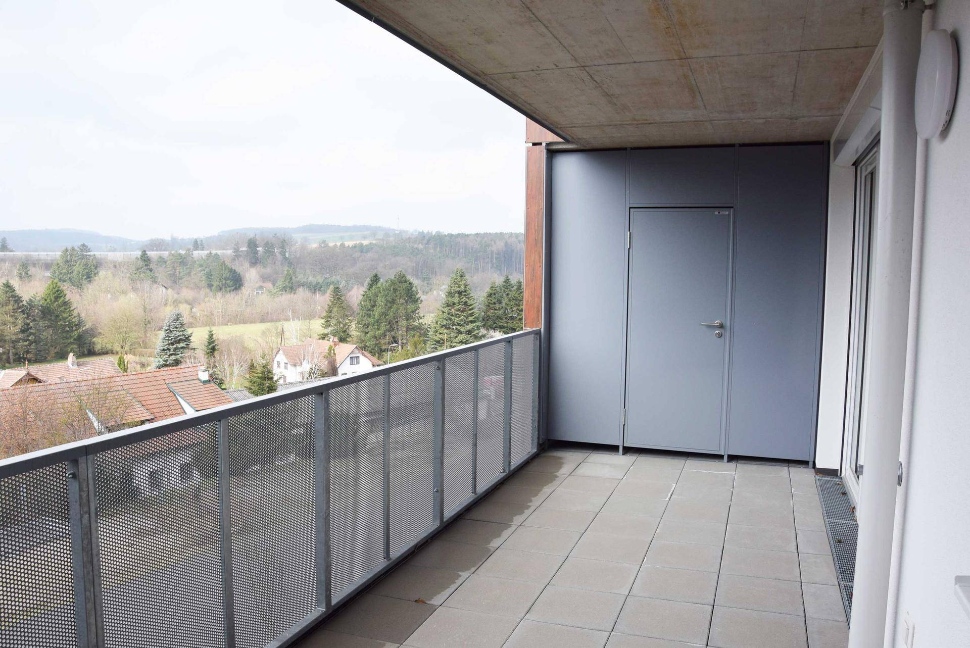 Geräumiger Balkon mit Fliesenboden und weitem Blick über die grüne Landschaft und Häuser.