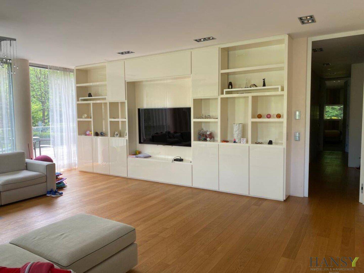 Heller Wohnbereich mit integrierter weißer Schrankwand und Holzboden, ideal für Unterhaltung.