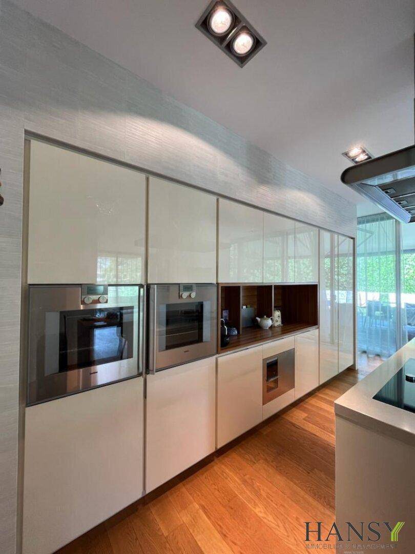 Elegante Küche mit weißen Hochglanzfronten, integrierten Geräten und Holzboden.