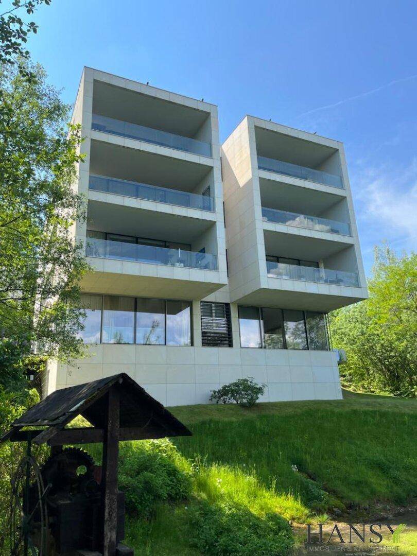 Moderne Architektur mit mehreren Balkonen und großen Glasflächen, umgeben von viel Grün.
