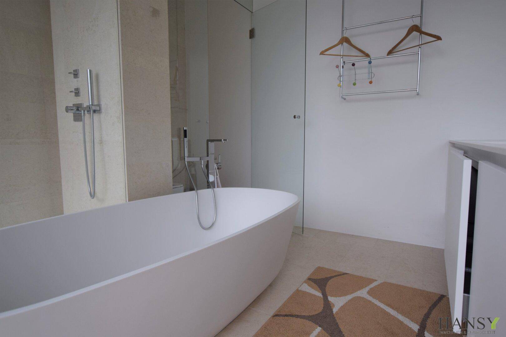 Modernes Badezimmer mit freistehender Badewanne und begehbarer Dusche, hell gefliest.