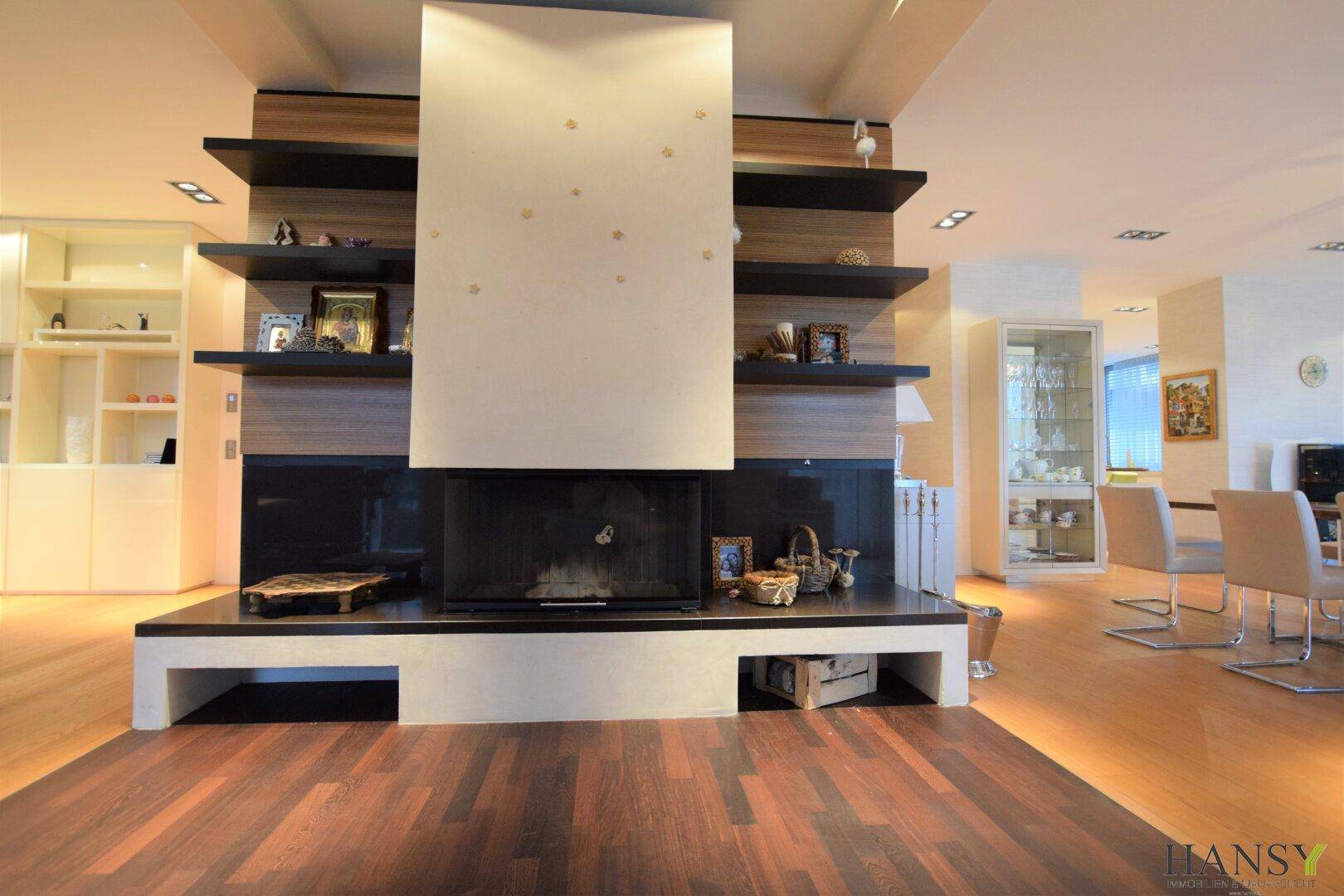 Moderner Kamin als Raumteiler mit Holzverkleidung und dunklem Holzboden im Wohnbereich.