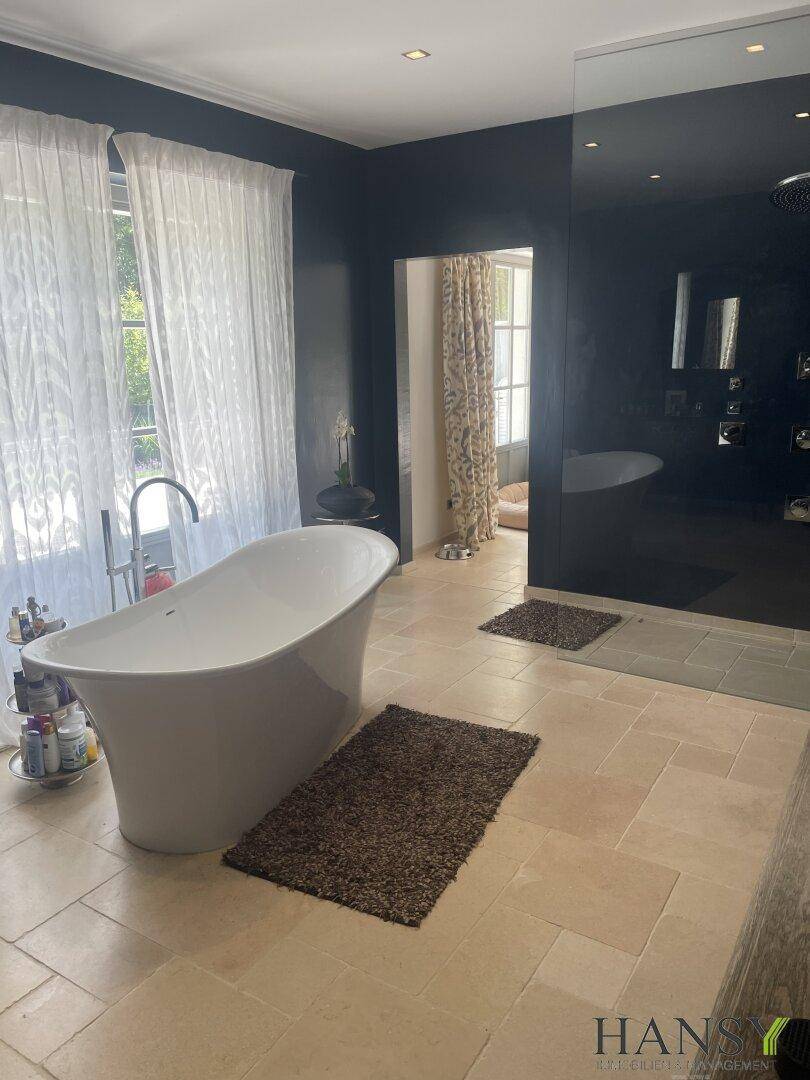 Geräumiges Badezimmer mit freistehender Badewanne, begehbarer Dusche und Blick ins Grüne.