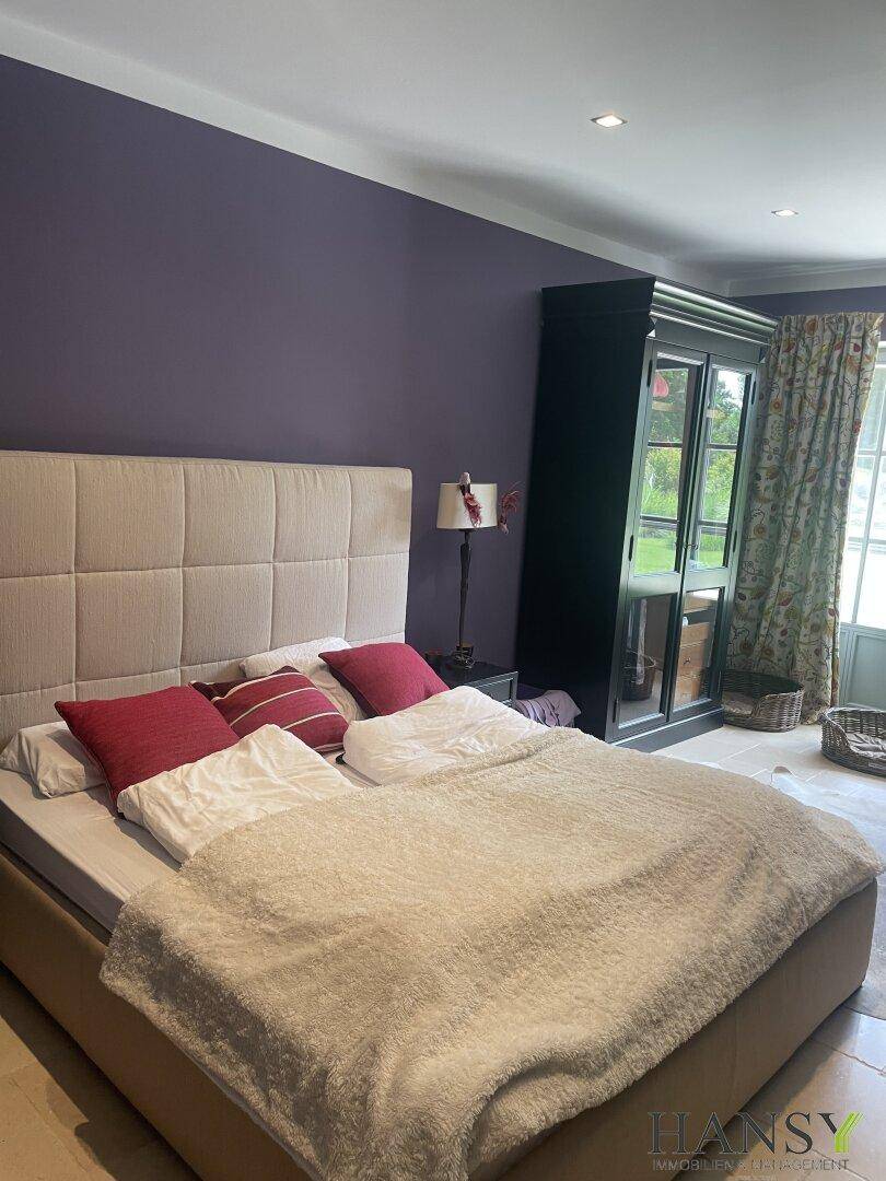 Helles Schlafzimmer mit lila Akzentwand, großem Bett und Blick in den Garten.
