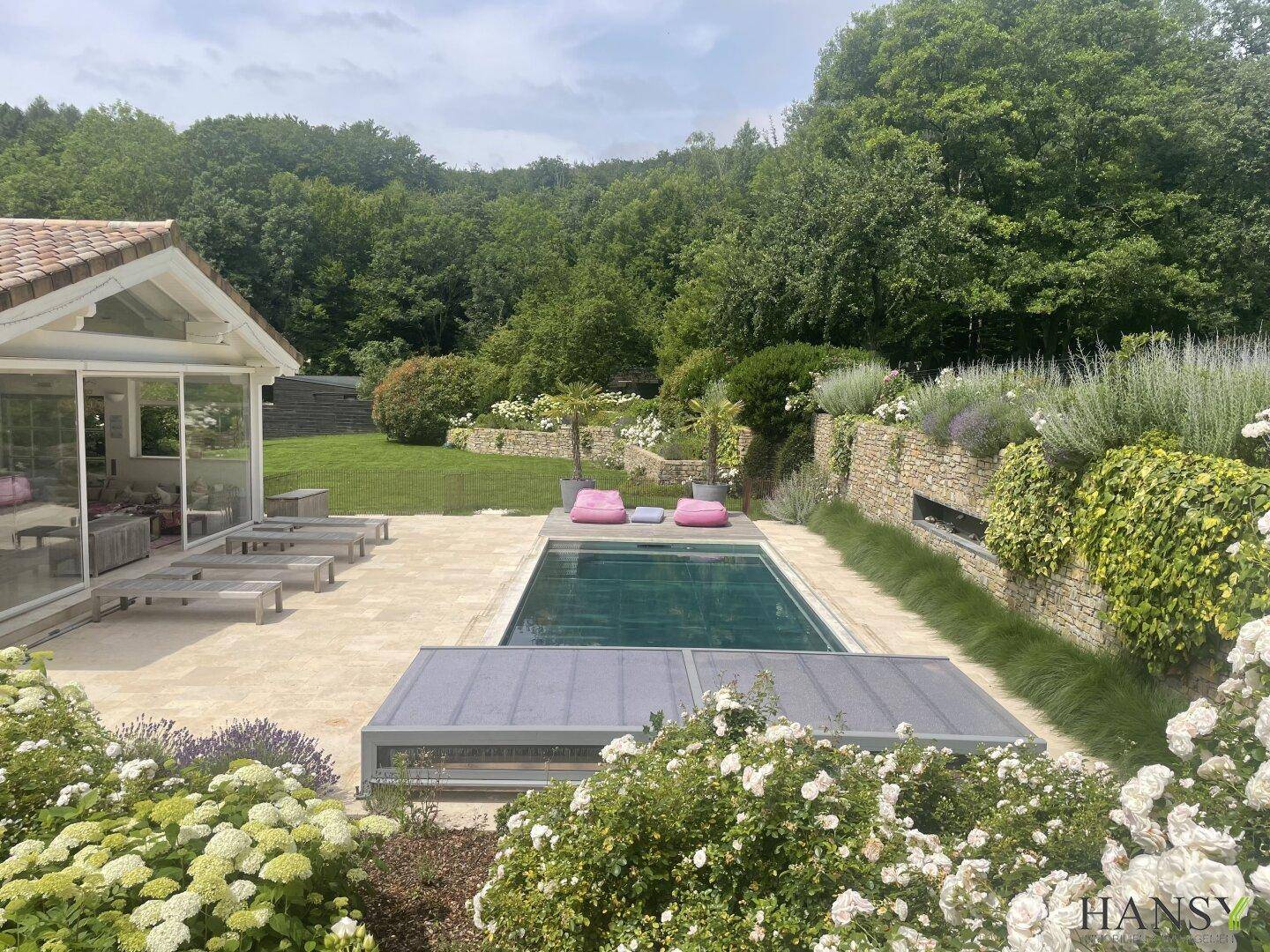 Malerischer Garten mit Pool, blühenden Pflanzen und Blick auf die bewaldete Umgebung.