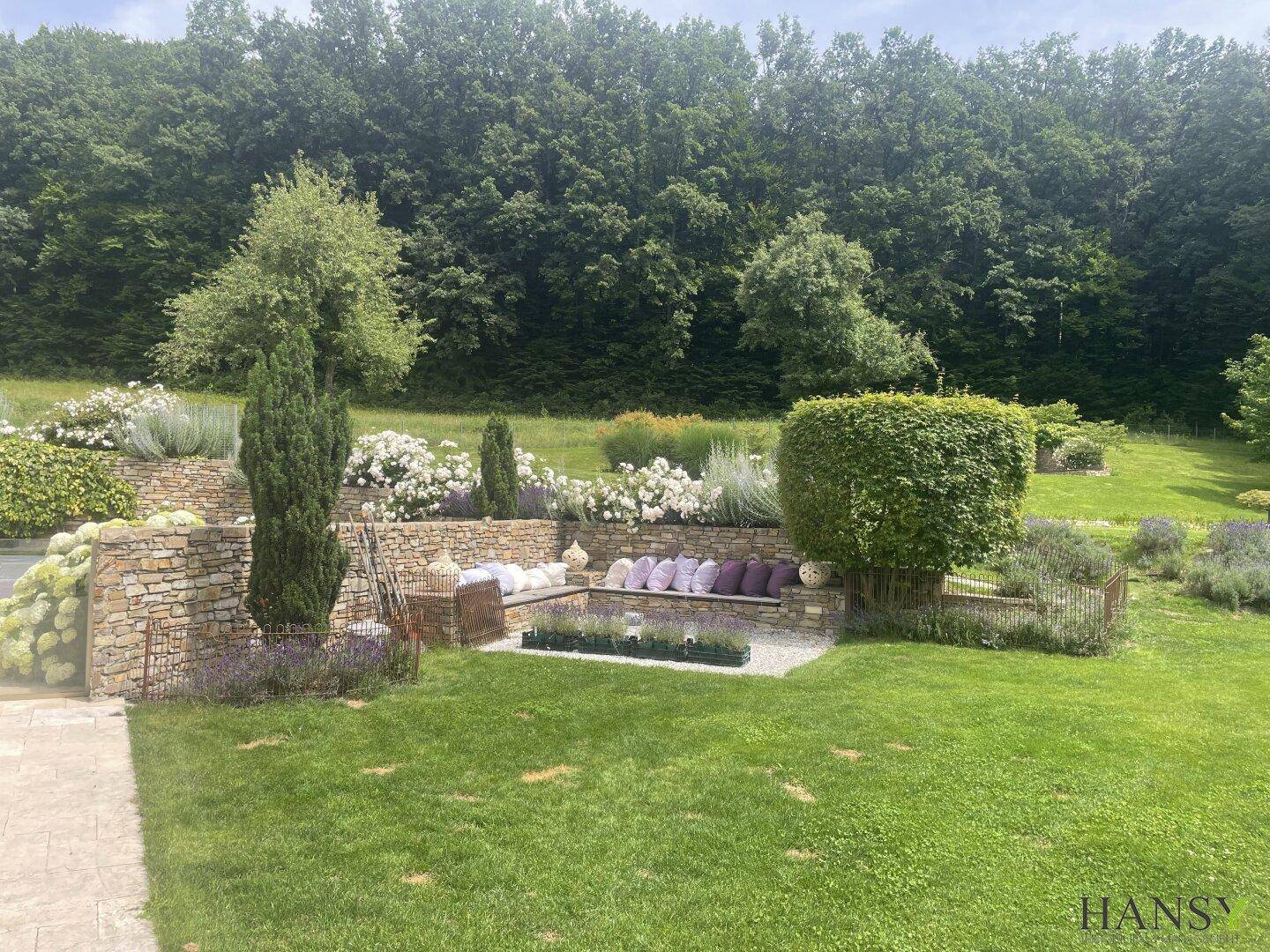 Weitläufiger Garten mit Rasenflächen, Steinmauern und einer gemütlichen Sitzecke im Freien.
