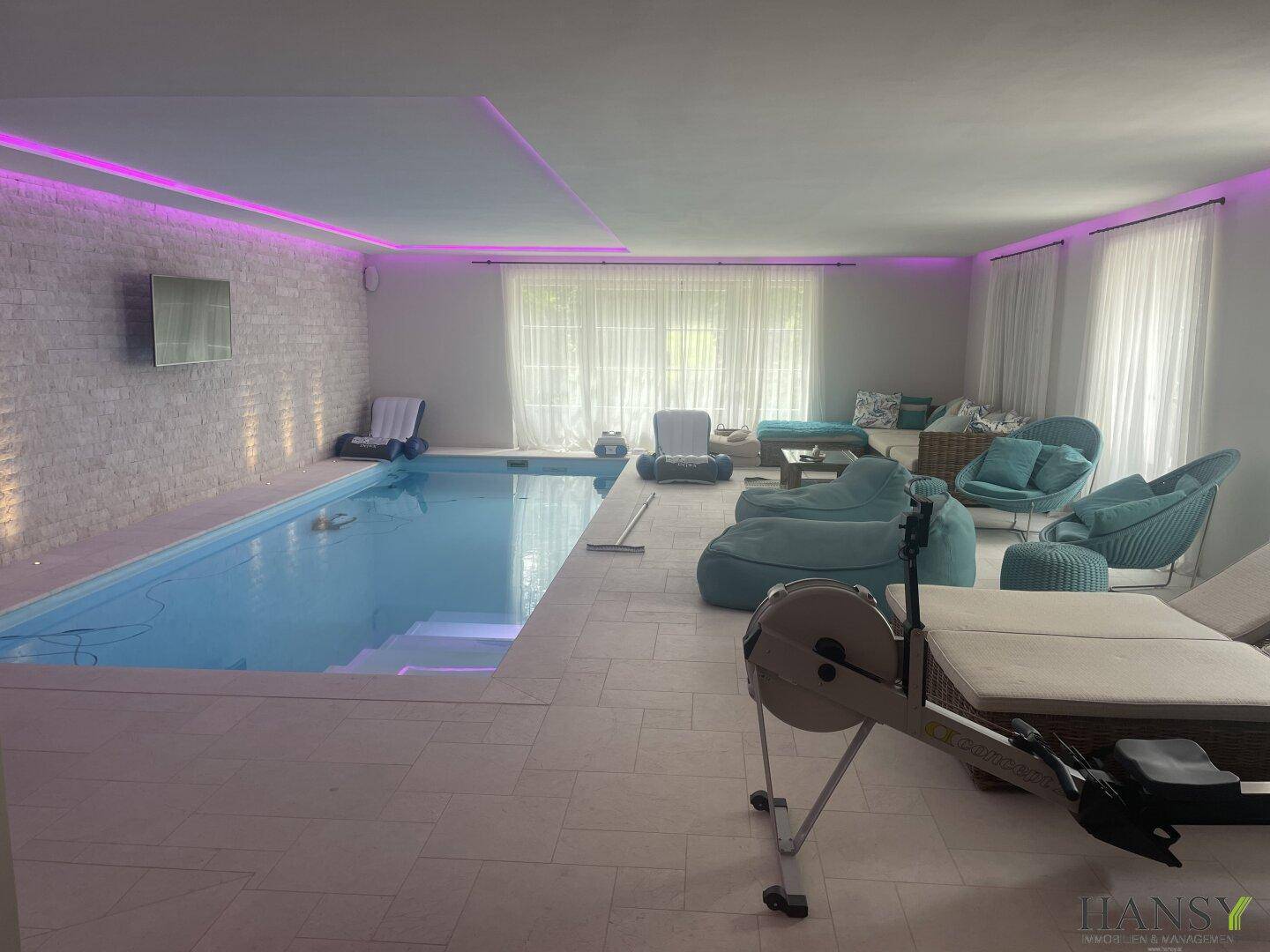 Geräumiger Innenpoolbereich mit Fitnessgeräten und Lounge-Möbeln, ideal für Sport und Entspannung.