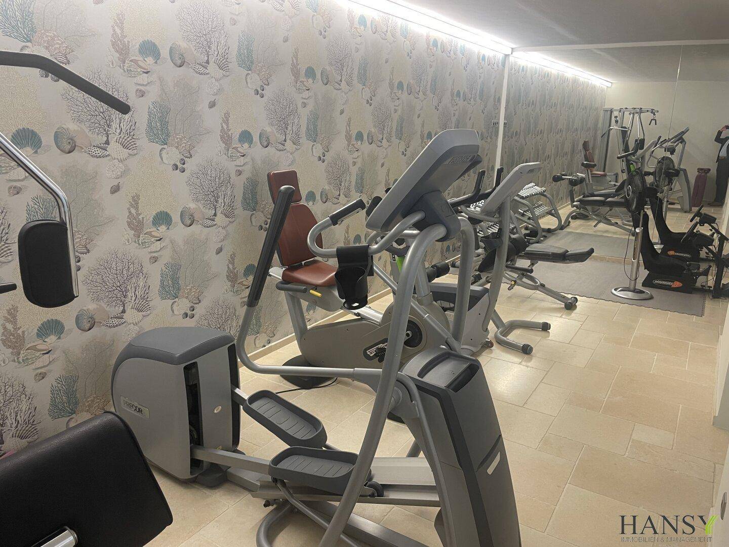Gut ausgestatteter Fitnessraum mit verschiedenen Trainingsgeräten und dekorativer Tapete.