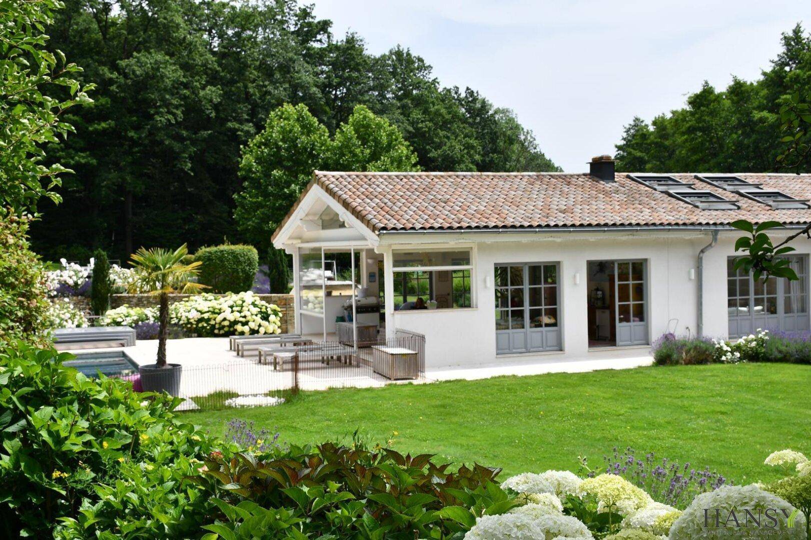 Das Landhaus vom Garten aus gesehen, mit überdachter Terrasse und dem angrenzenden Poolbereich.
