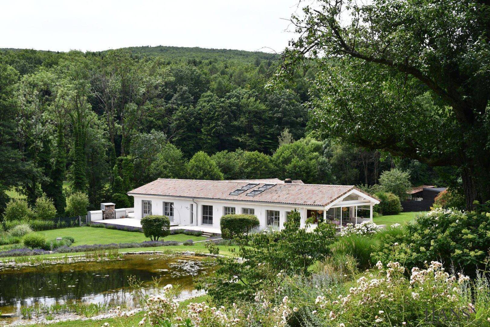 Weitläufiger Blick auf das charmante Landhaus, umgeben von einem großen Garten und dichtem Wald.