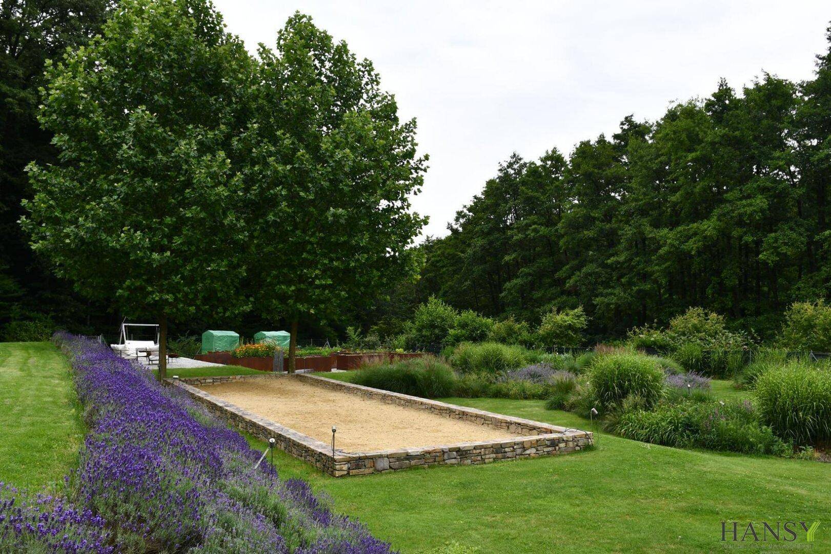 Großer Garten mit Bouleplatz, Lavendelreihen und umgebenden Wäldern.