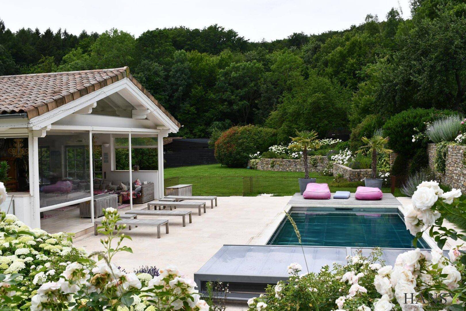 Attraktives Anwesen mit Pool, Sonnenterrasse und blühenden Rosen im Vordergrund.