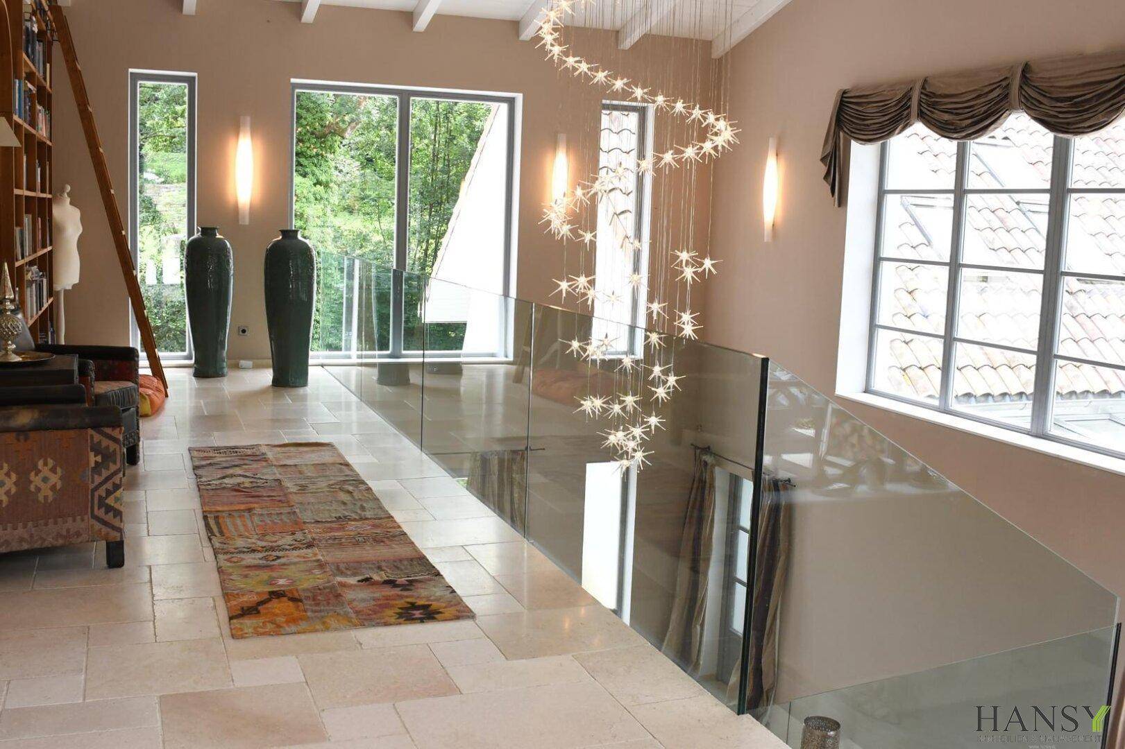 Heller Galeriebereich im Obergeschoss mit großen Fenstern, Blick ins Grüne und einem dekorativen Teppich.