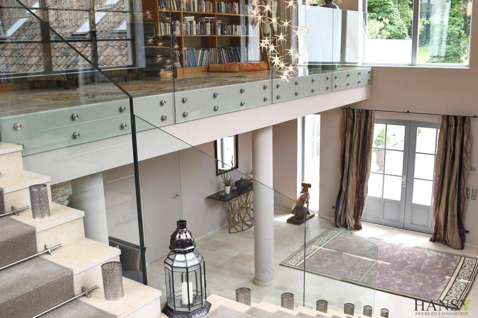 Blick von der Galerie auf den Eingangsbereich mit eleganter Treppe und großem Teppich.