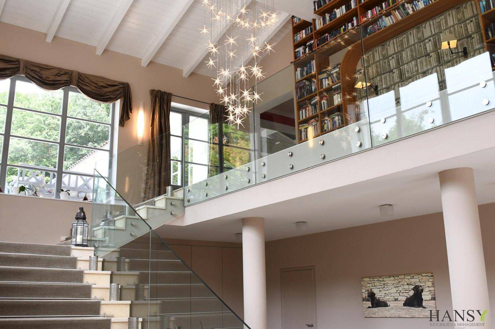 Großzügiger Eingangsbereich mit eleganter Treppe, Glasgeländer und beeindruckendem Kronleuchter.