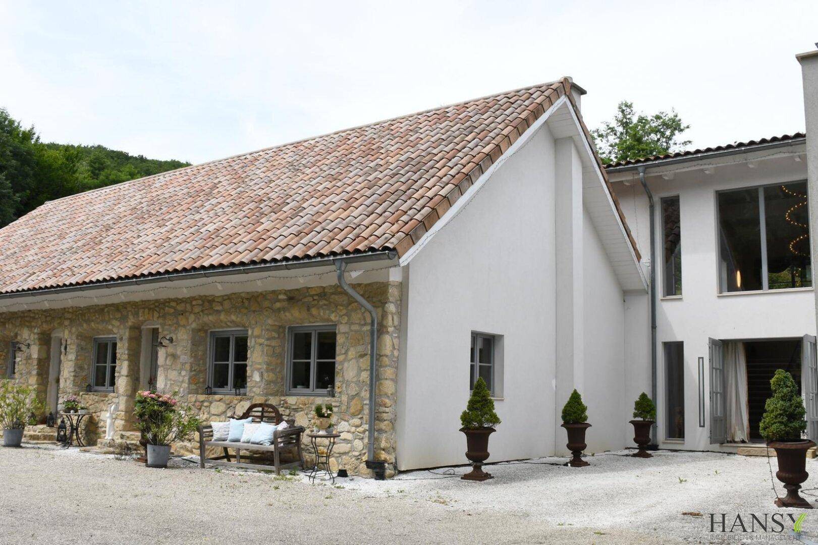 Seitenansicht des Hauses mit einer Kombination aus rustikaler Steinfassade und modernem weißem Putz.